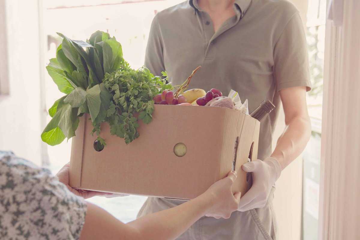 A person distributing food from a box of fruit and vegetables for food support programs.