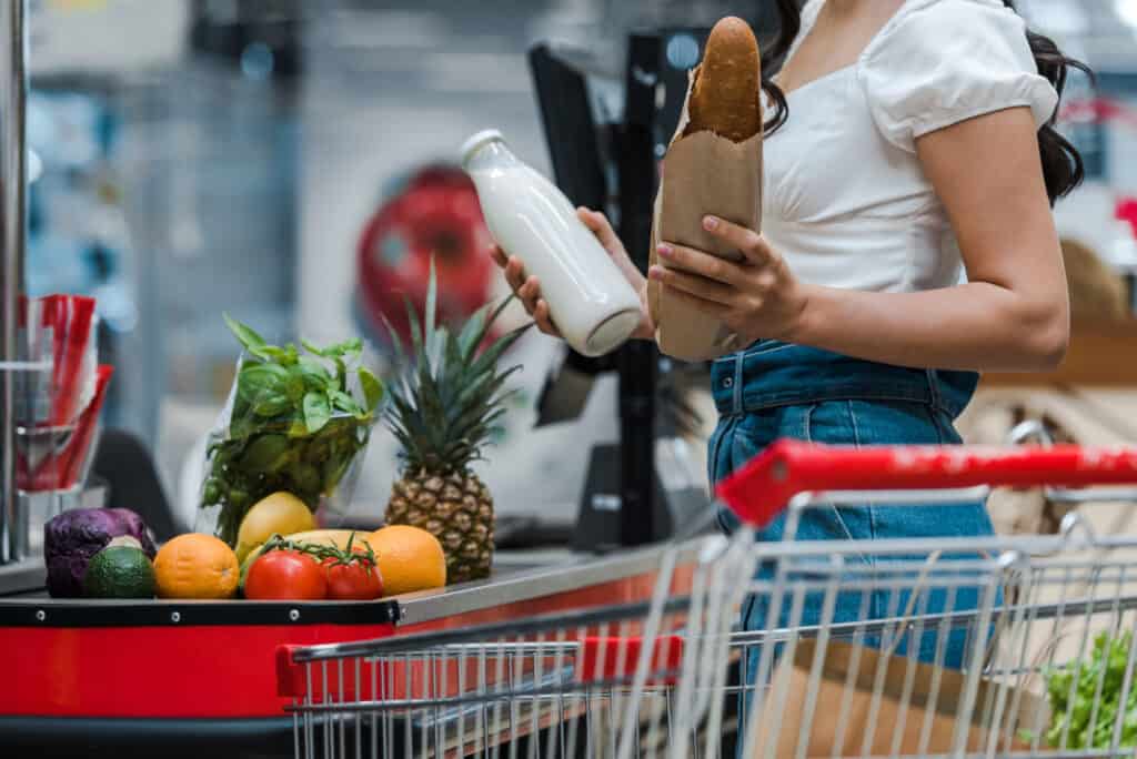 A woman using EBT holding a container of food in a grocery store.