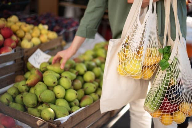 A woman is holding a shopping bag full of fruits and vegetables.