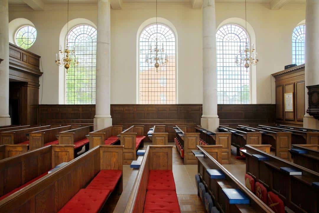 The interior of a church with wooden pews and large windows.