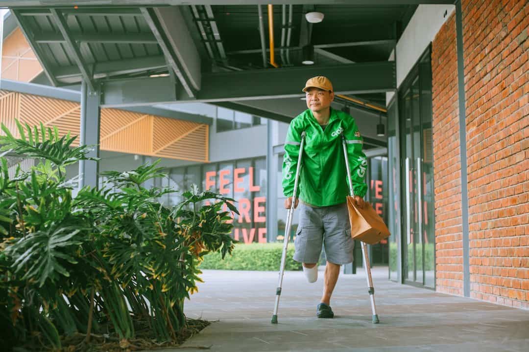 A man with crutches walking down a sidewalk.